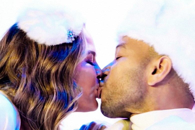 Chrissy Teigen and John Legend kiss while wearing Santa outfits.